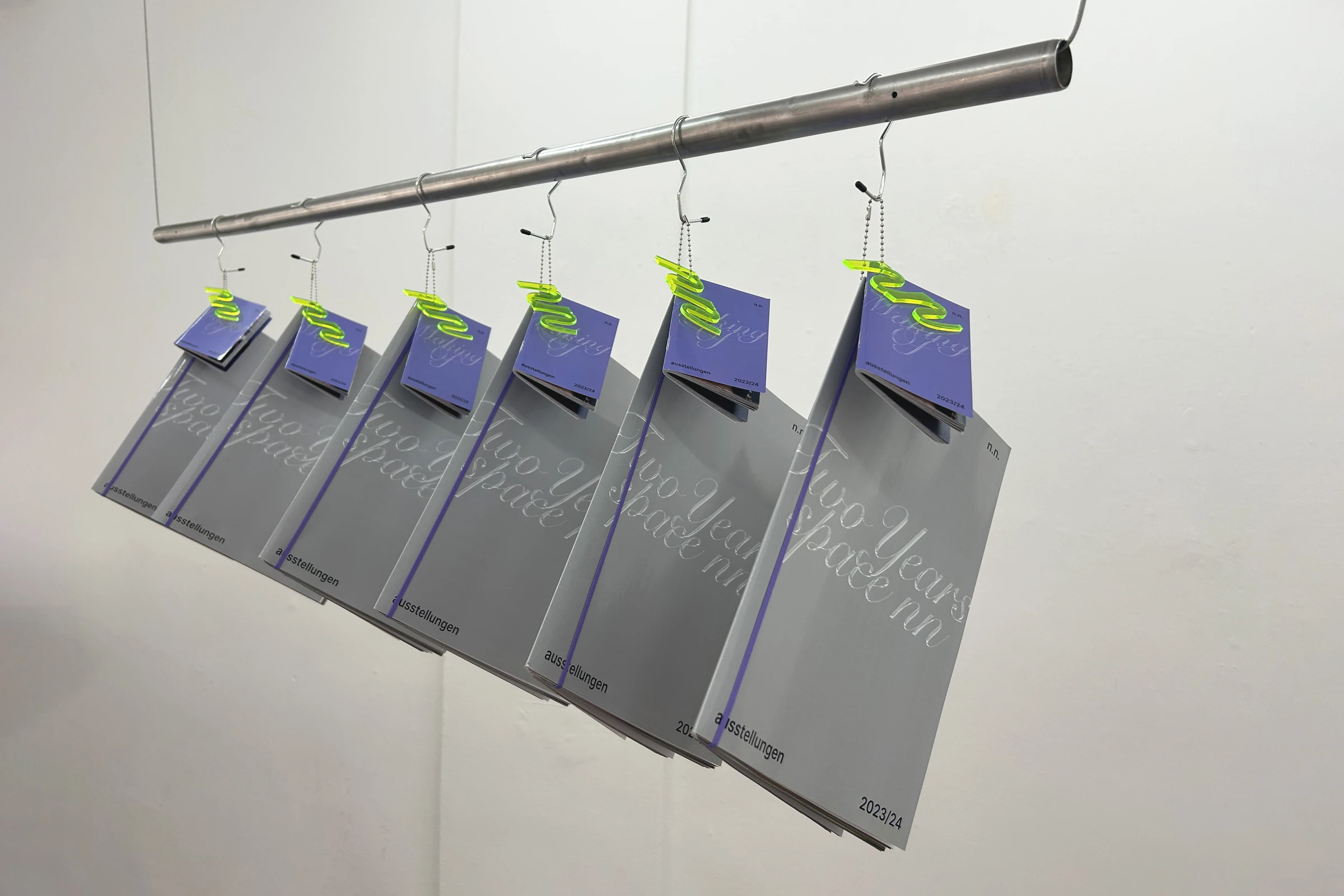 Catalogs hanging from hooks on a metal rail in a gallery