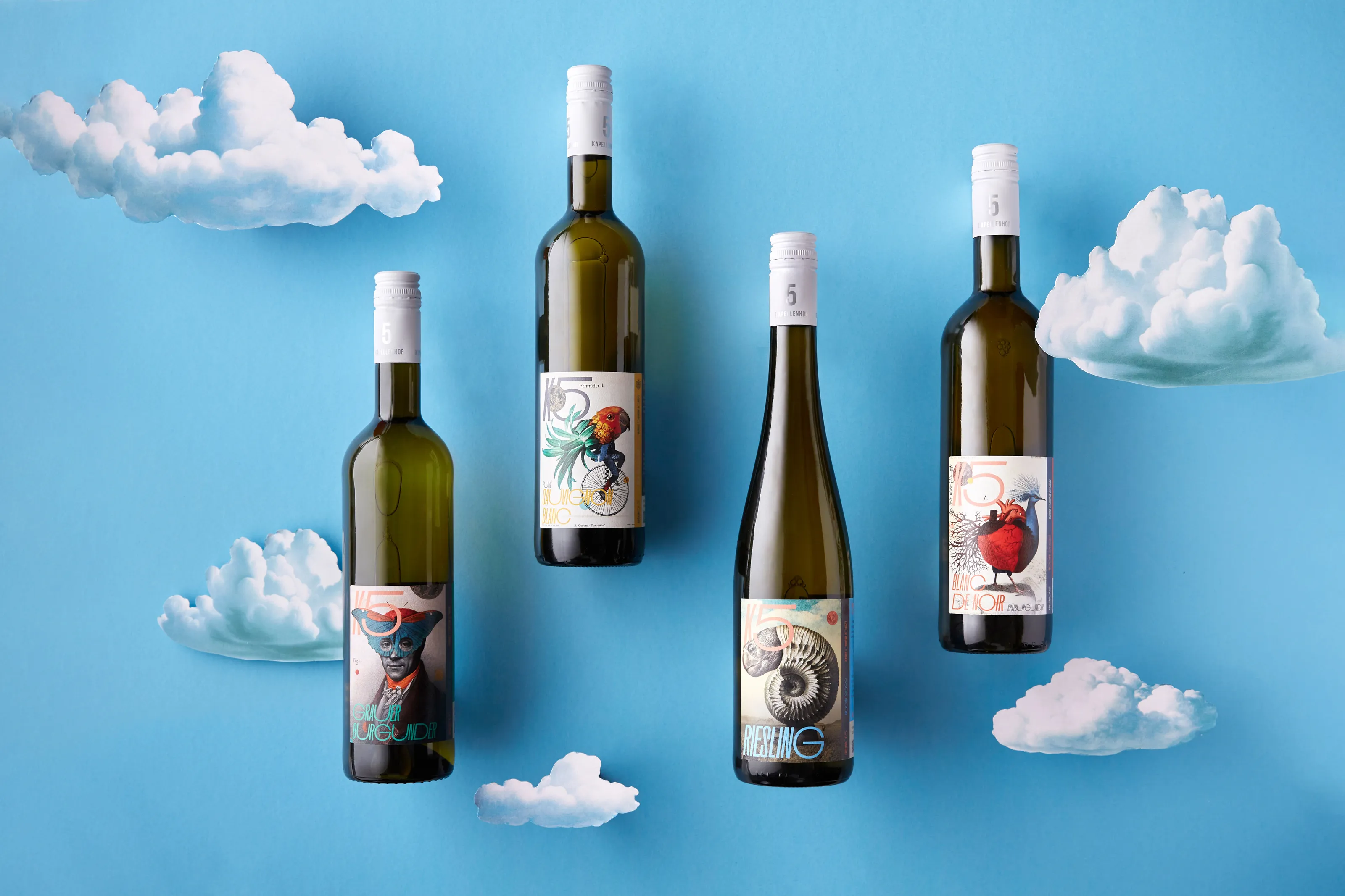 Four wine bottles with collage labels floating among white clouds on a sky-blue background
