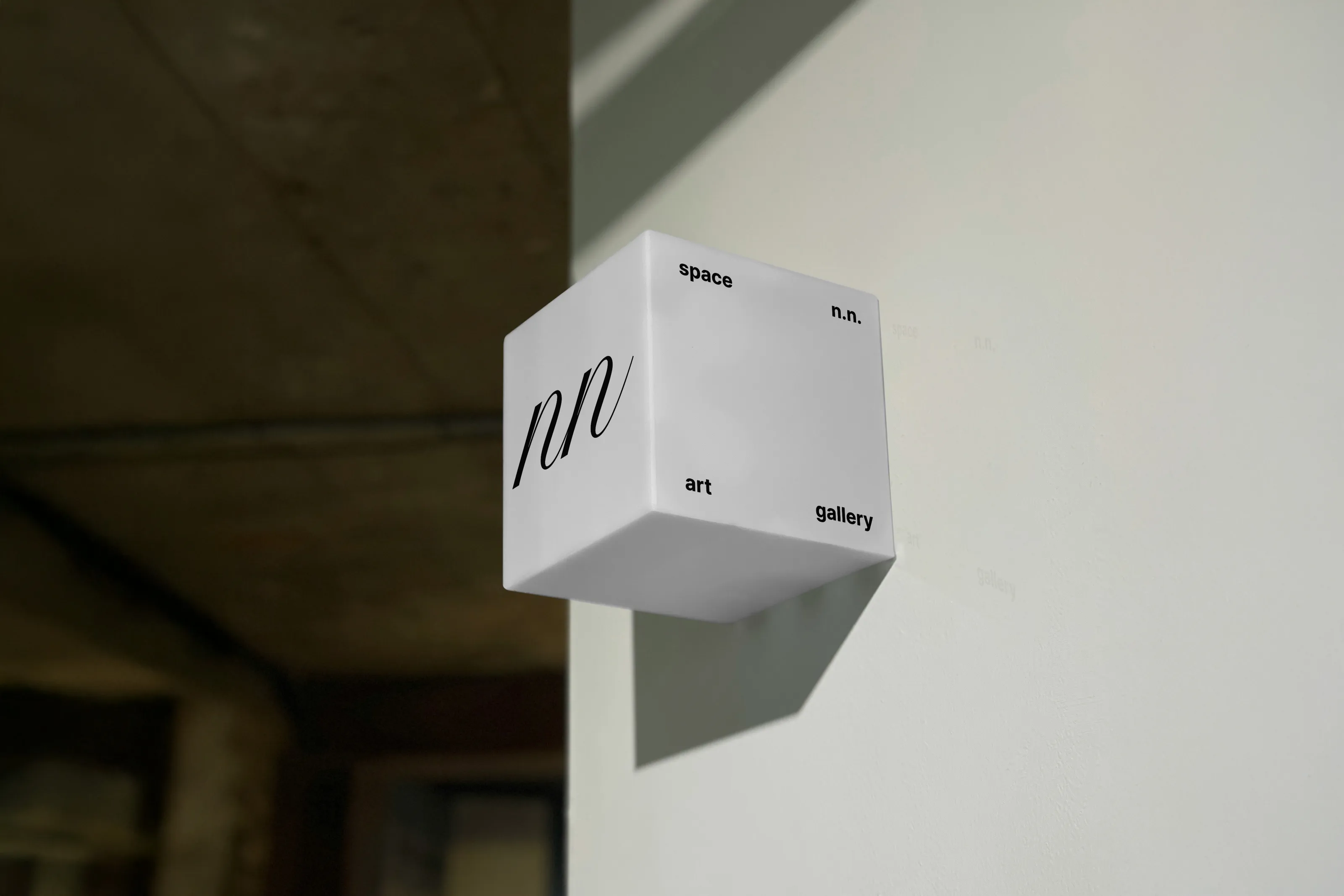White cube-shaped sign on a wall with the space n.n. logo