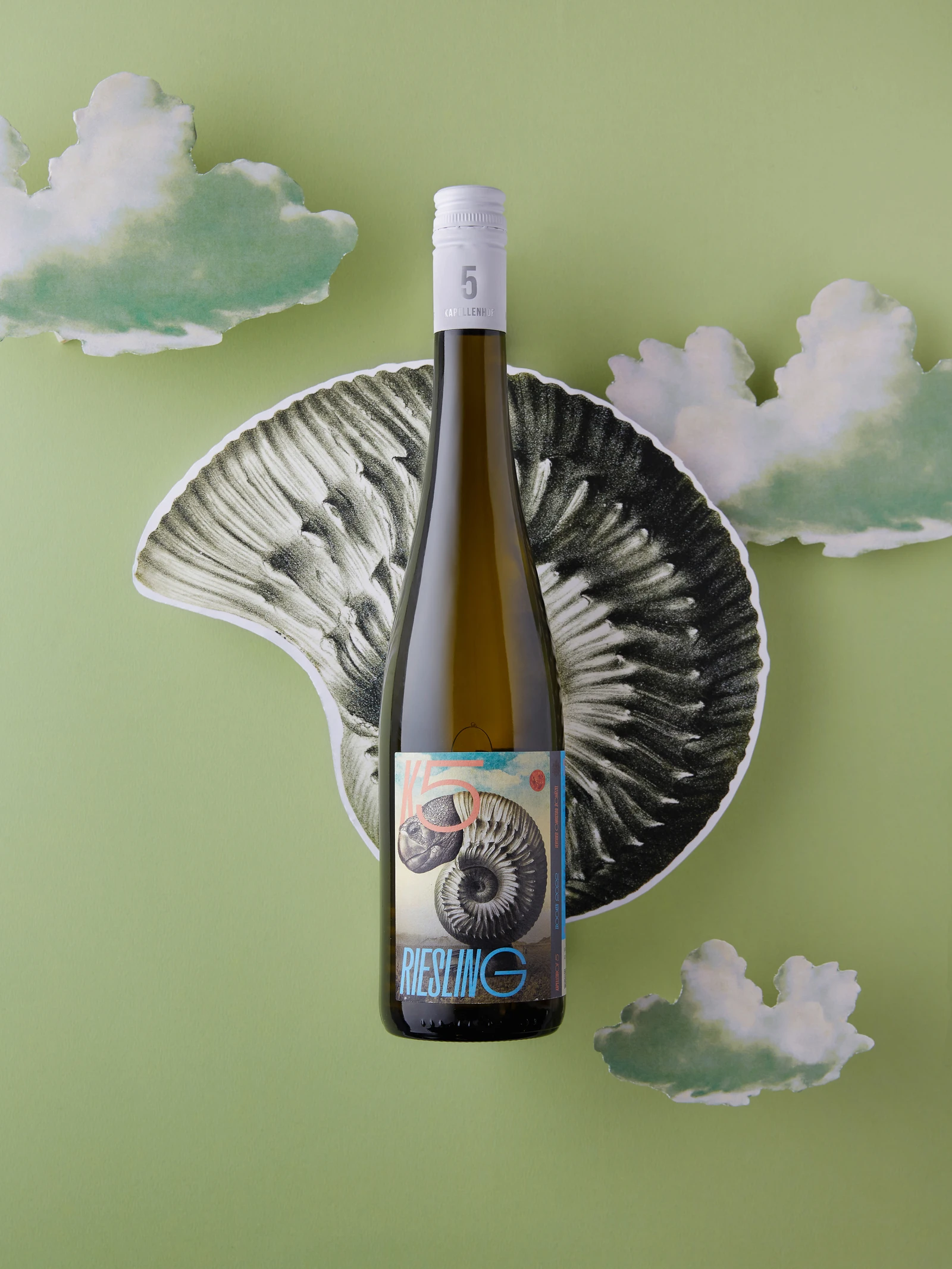 Riesling bottle with an ammonite label in front of a large cut-out ammonite and clouds on green