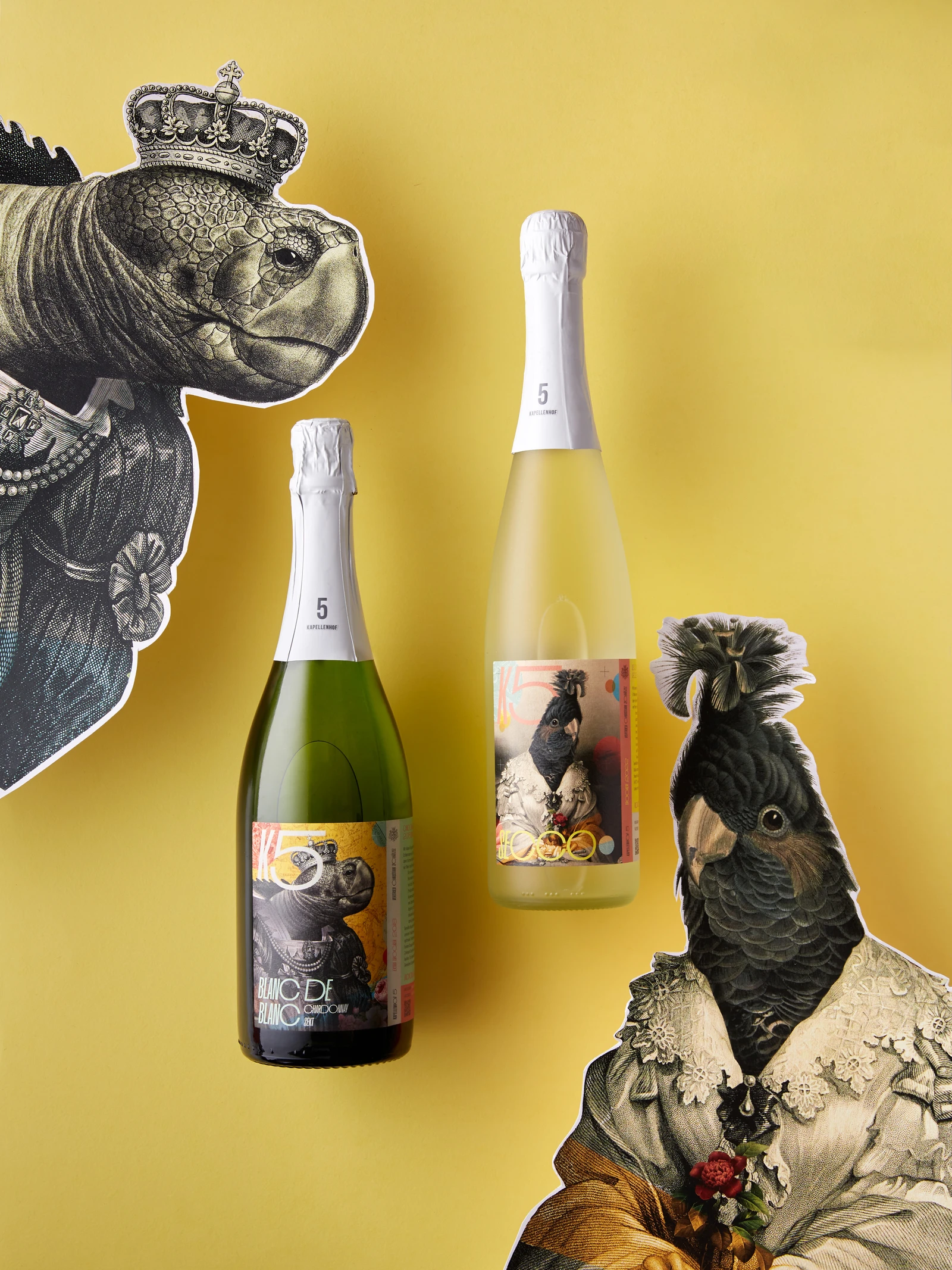 Two sparkling wine bottles on yellow between cut-out collage figures of a crowned tortoise and a cockatoo in a lace dress