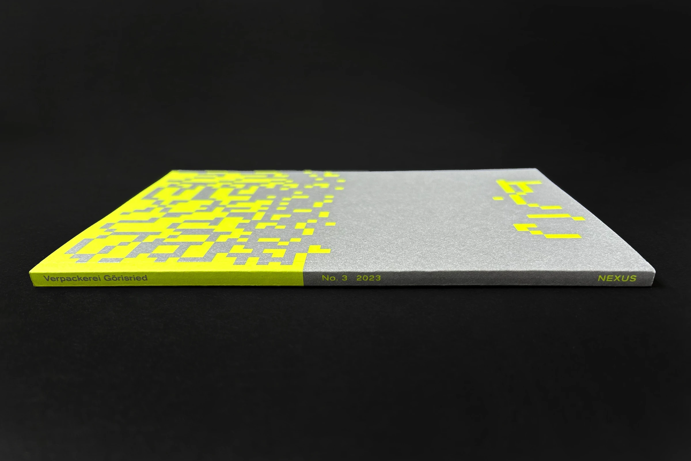 Catalog seen from the side, with a neon yellow and silver pixel pattern
