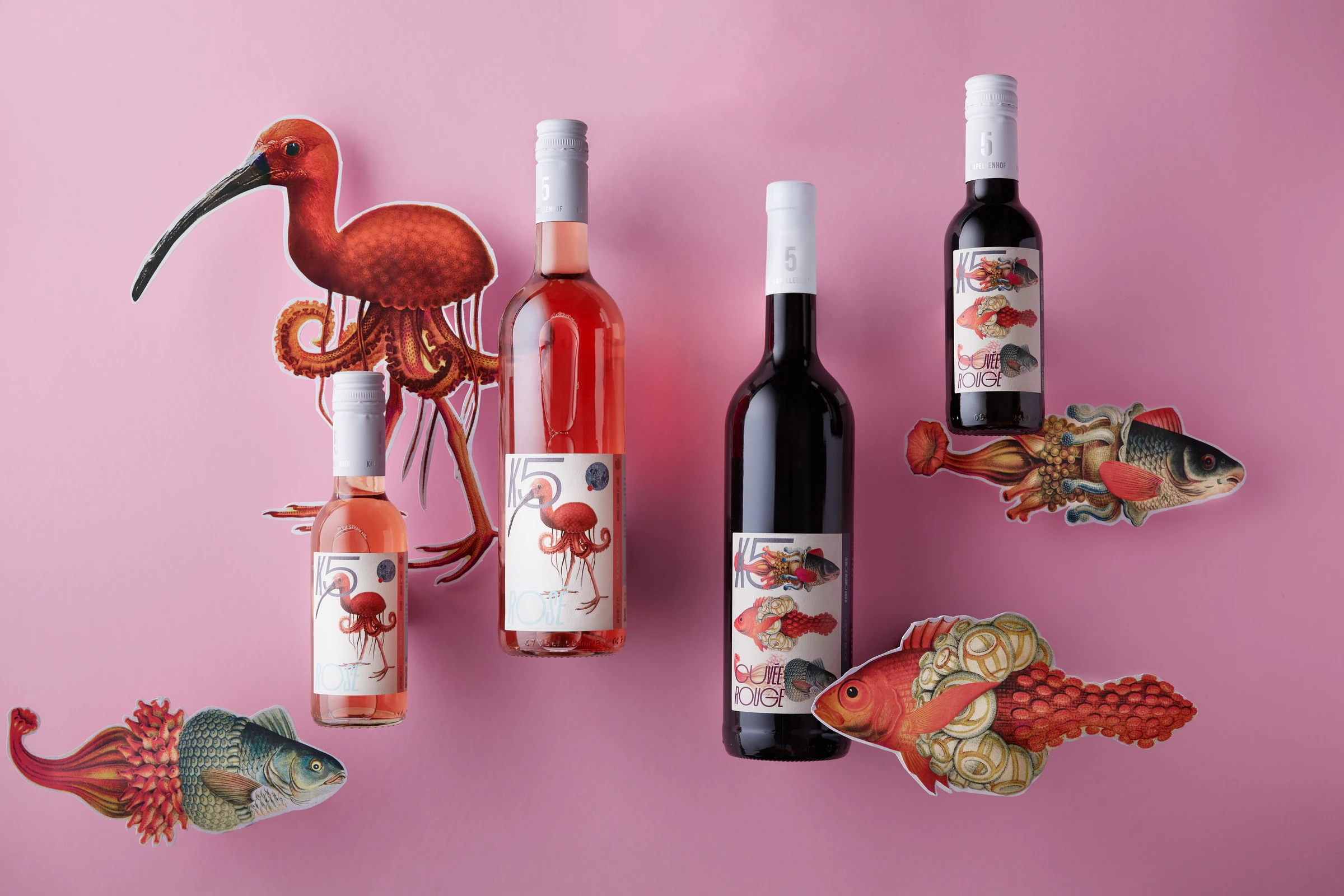 Rosé and red wine bottles on pink with cut-out collage creatures: an ibis with octopus legs and fish with ornate tails