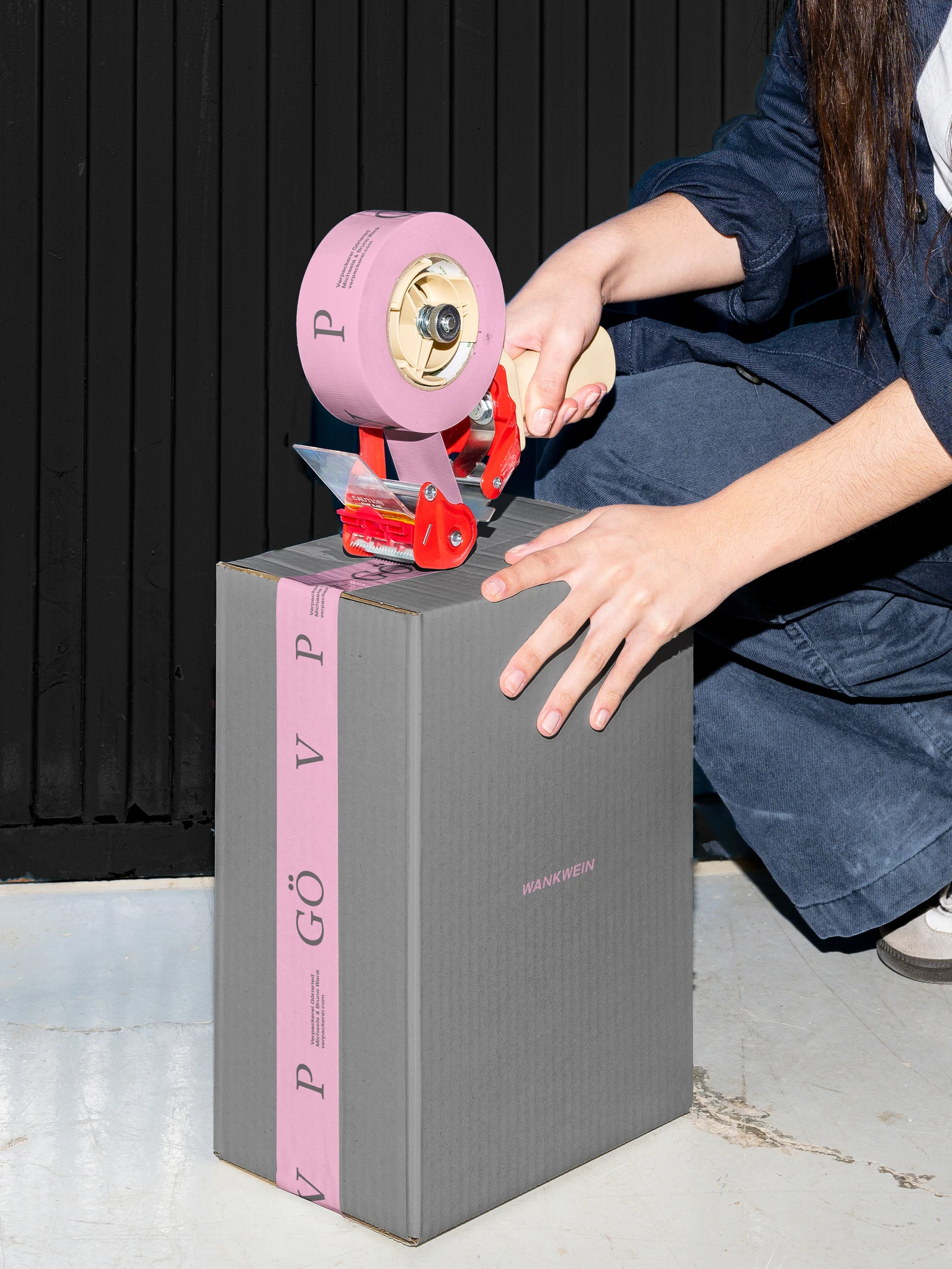 Person sealing a grey shipping box with pink VerpackereiGö tape
