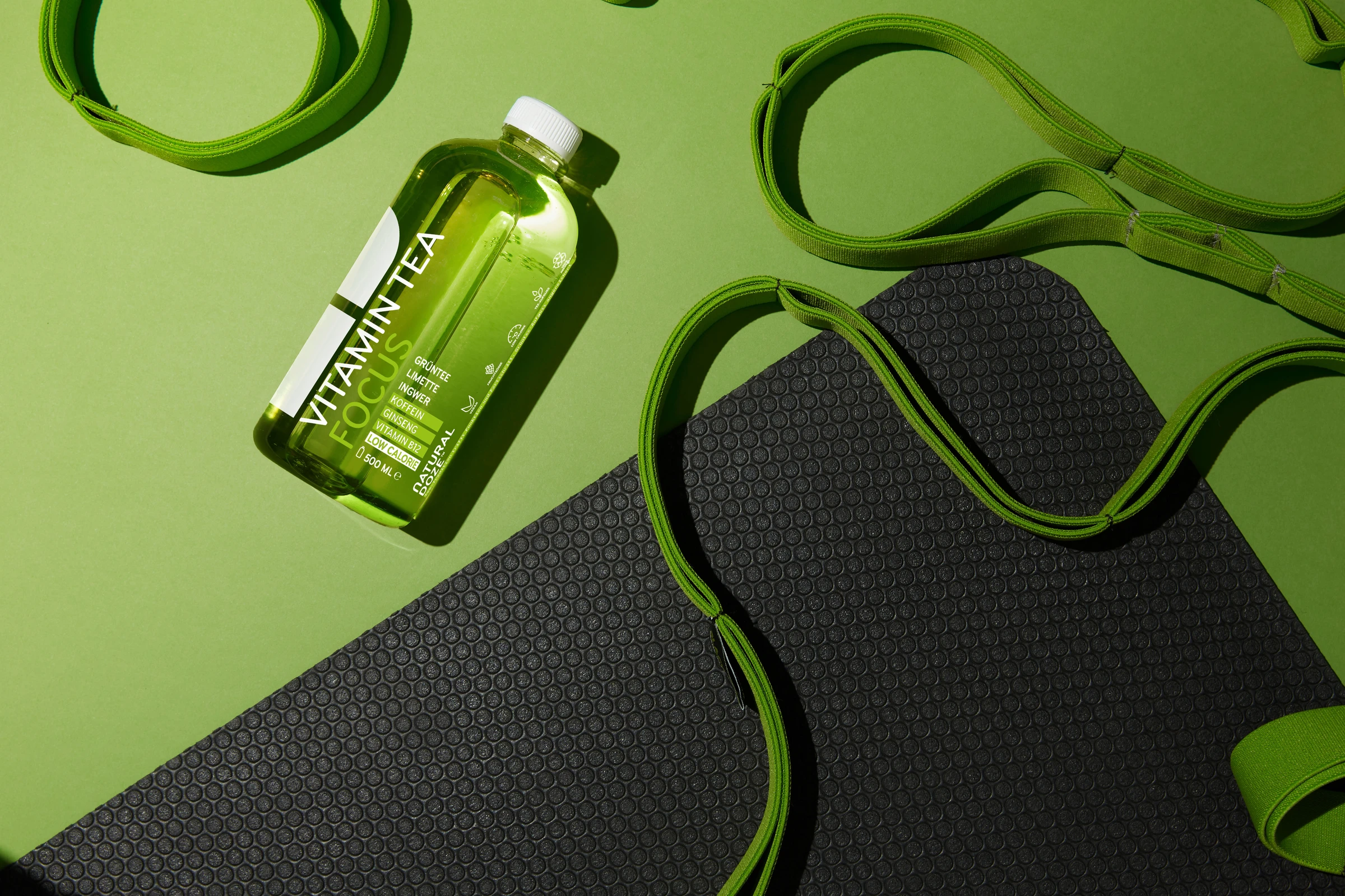 Green Vitamin Tea bottle lying next to a resistance band and an exercise mat
