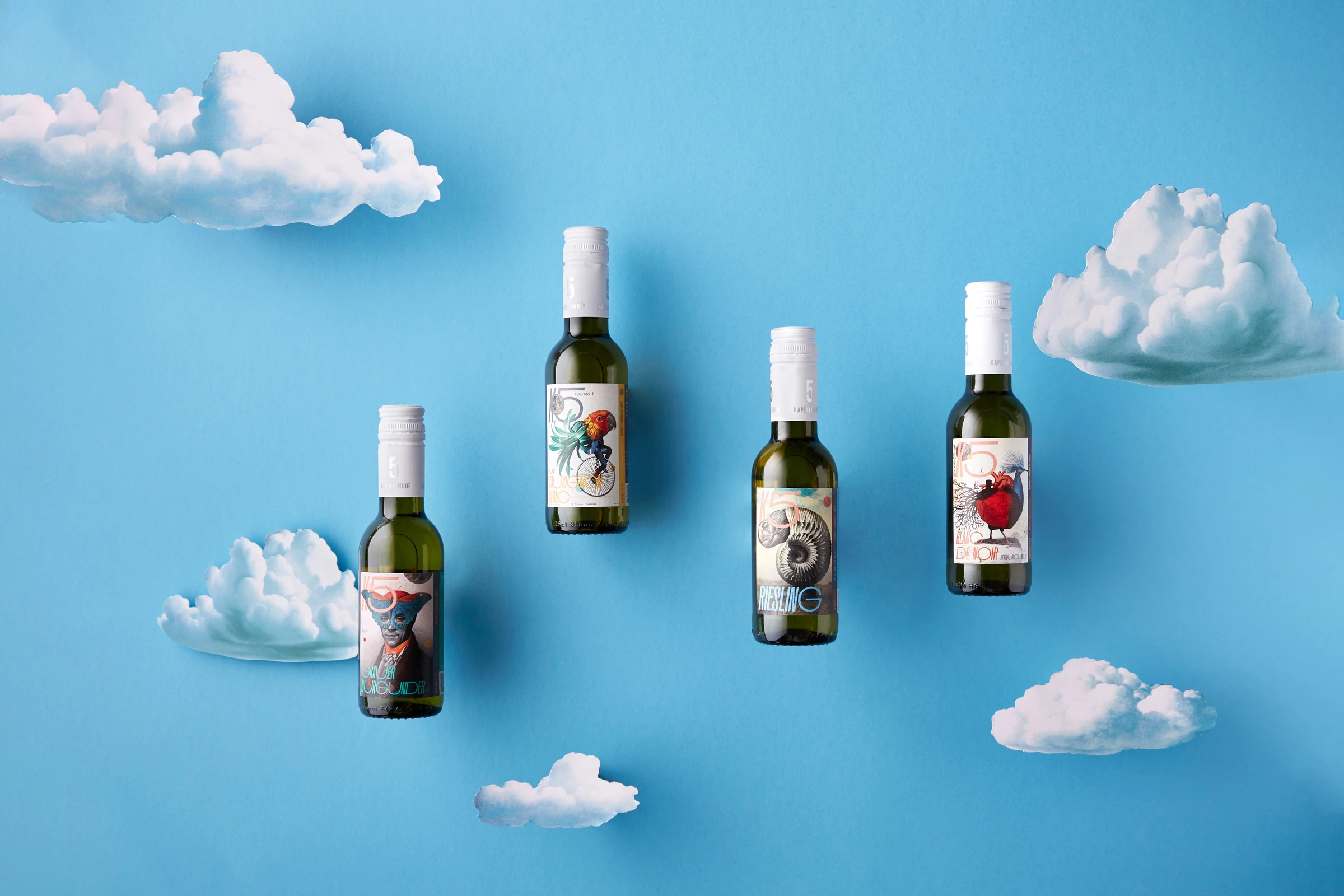 Four small wine bottles with collage labels floating among white clouds on a sky-blue background